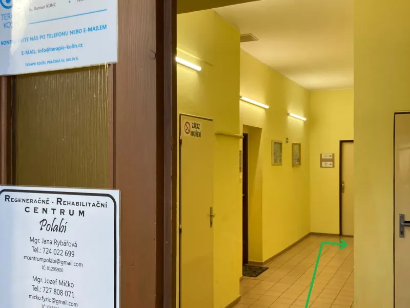 Otevřené prosklené dveře s cedulí centra, za nimi světlá chodba s několika dveřmi. Zelená šipka vede chodbou dál.