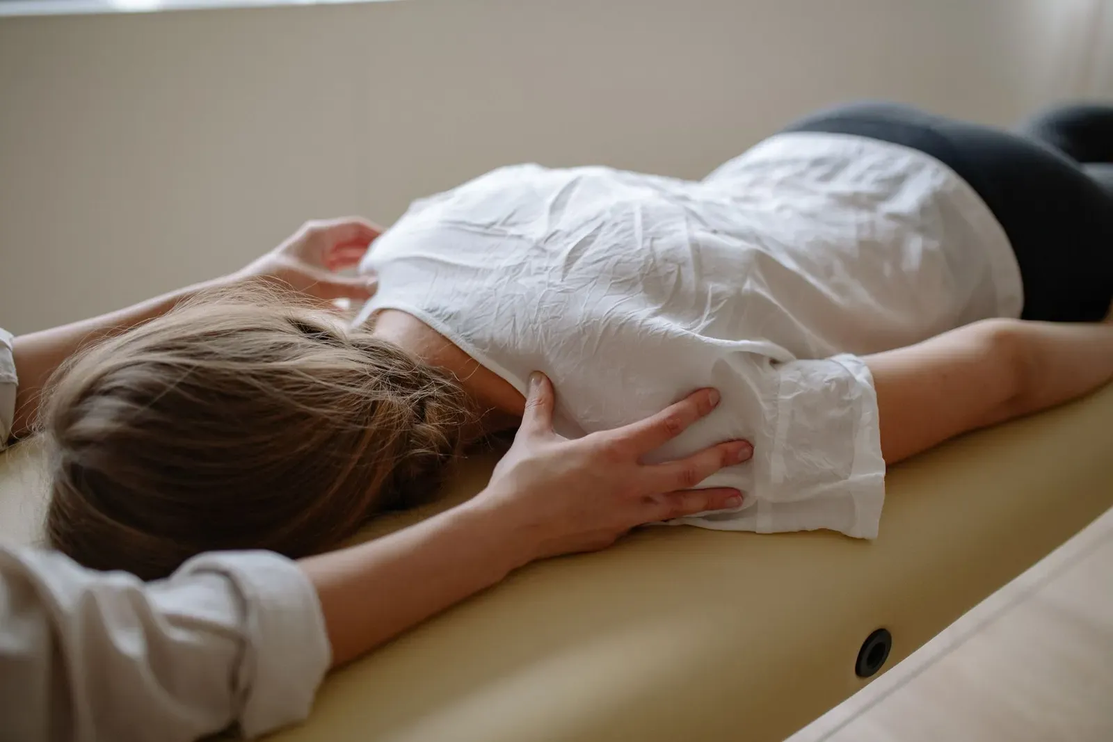 Klientka leží na břiše na lehátku, ruka terapeutky spočívá na jejích zádech